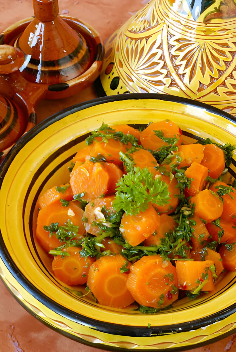 A vibrant bowl of traditional Moroccan carrot salad, made with finely sliced carrots, cumin, lemon juice, and olive oil, garnished with fresh cilantro and a sprinkle of paprika.