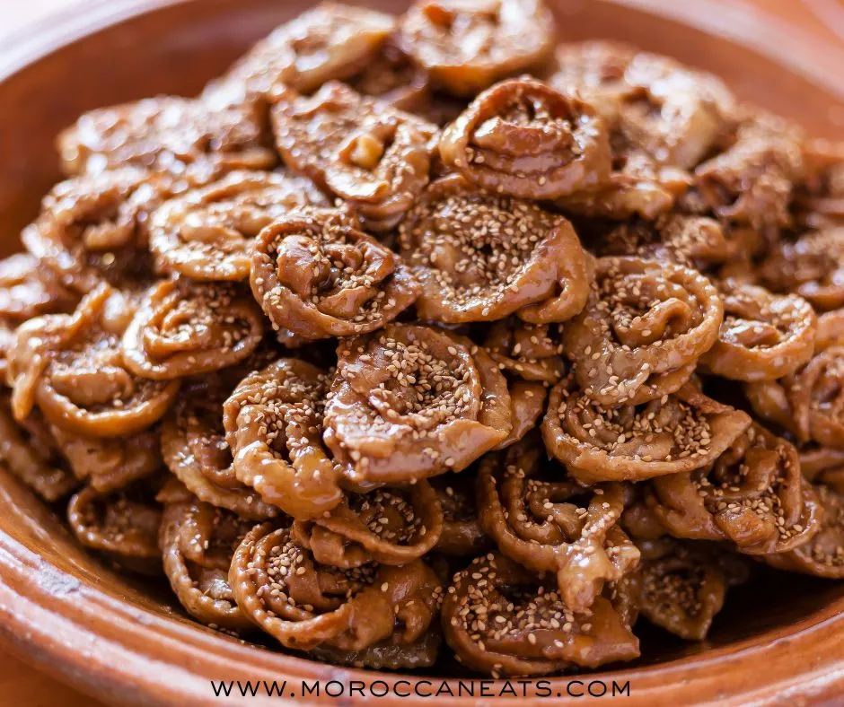Moroccan Dessert Chebakya : Addictive Sweet Sensation 2 Golden Moroccan dessert Chebakya pastries soaked in honey and topped with sesame seeds, served on a traditional silver tray.