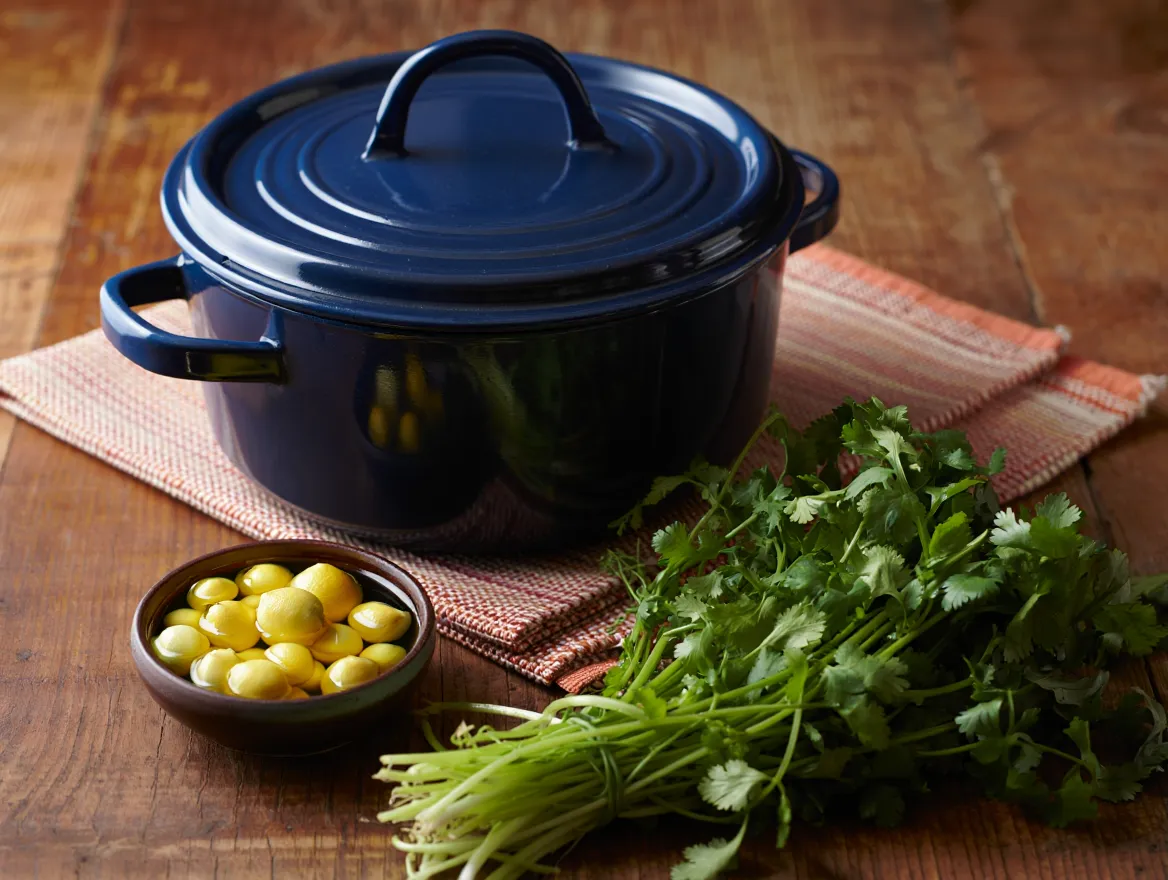 A heavy Dutch oven, symbolizing the ideal cooking pot, next to a jar of preserved lemons on a wooden table, illustrating pro-tips for making Cauliflower and Chickpeas Tagine.