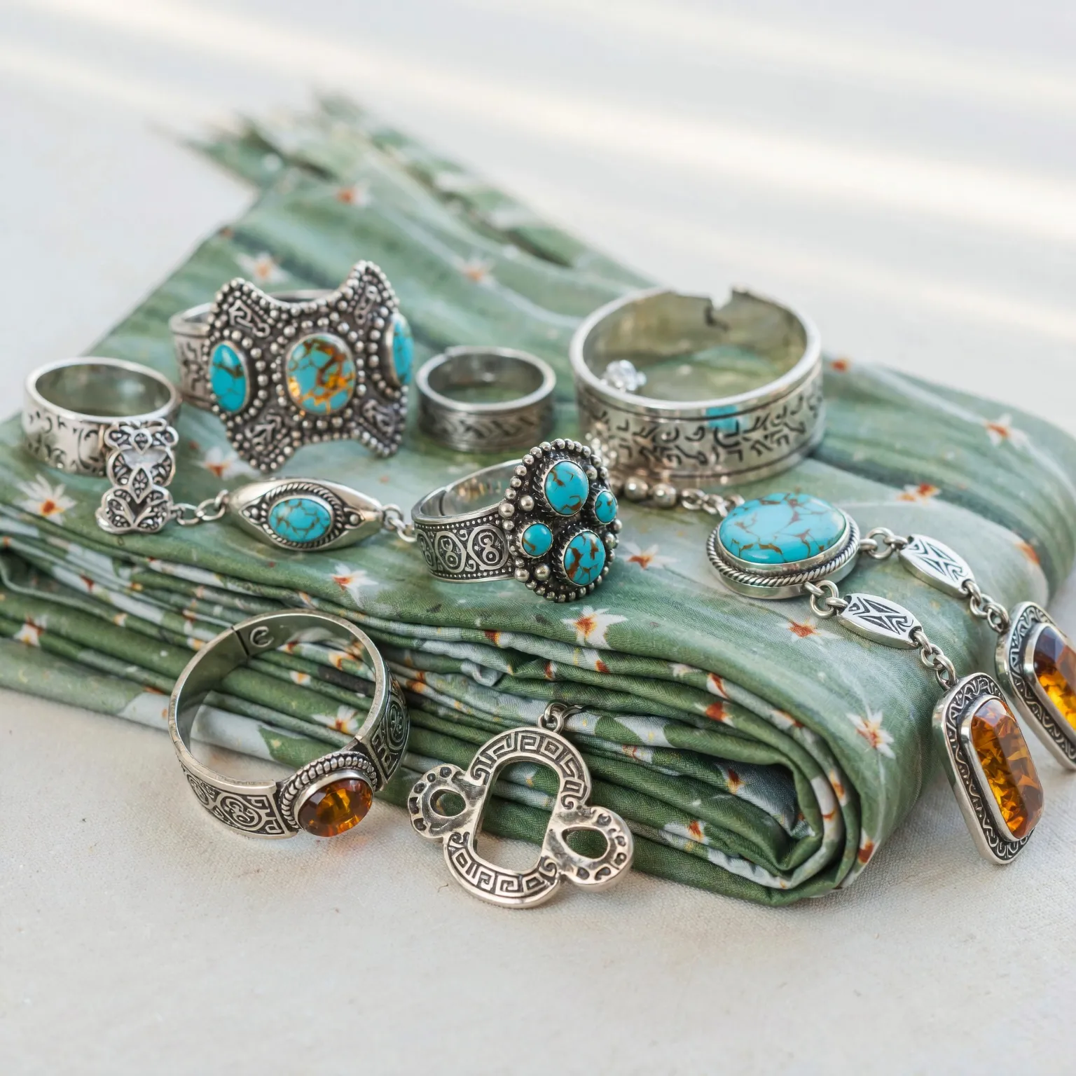 "A display of handcrafted Berber silver jewelry, including Khamsa pendants and rings, resting on a brightly colored cactus silk scarf."