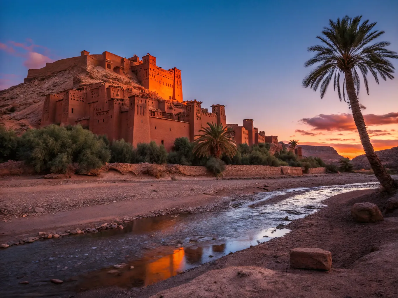 UNESCO World Heritage Sites in Morocco: Best & Magical 5 The fortified earthen village of Ait-Ben-Haddou glowing in the sunrise, showcasing traditional Moroccan clay architecture against a blue sky.