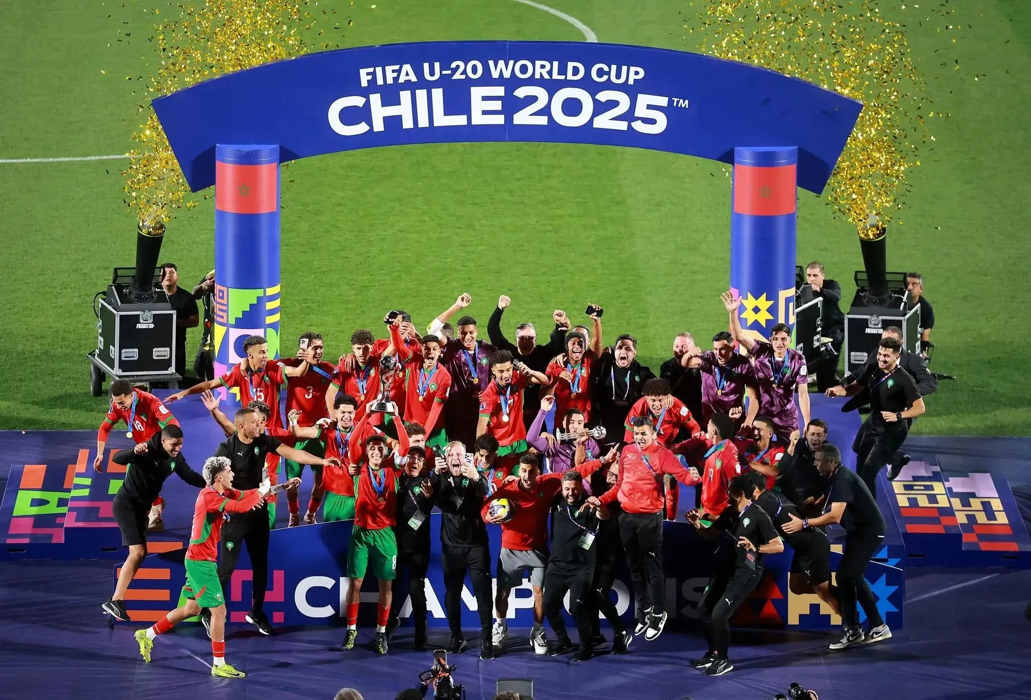 The Moroccan U-20 football team celebrating their historic 2025 World Cup victory, lifting the gold trophy amidst falling confetti in a packed stadium.